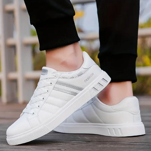 White sneakers with gray stripes worn by a person on a blurred outdoor background
